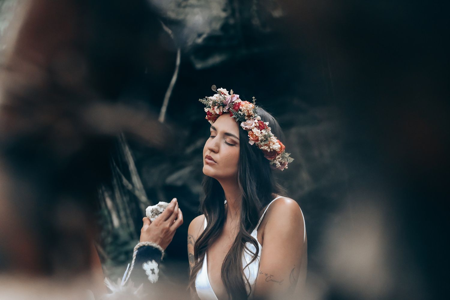 Floral crown adorns participant during traditional ceremony in forest setting.