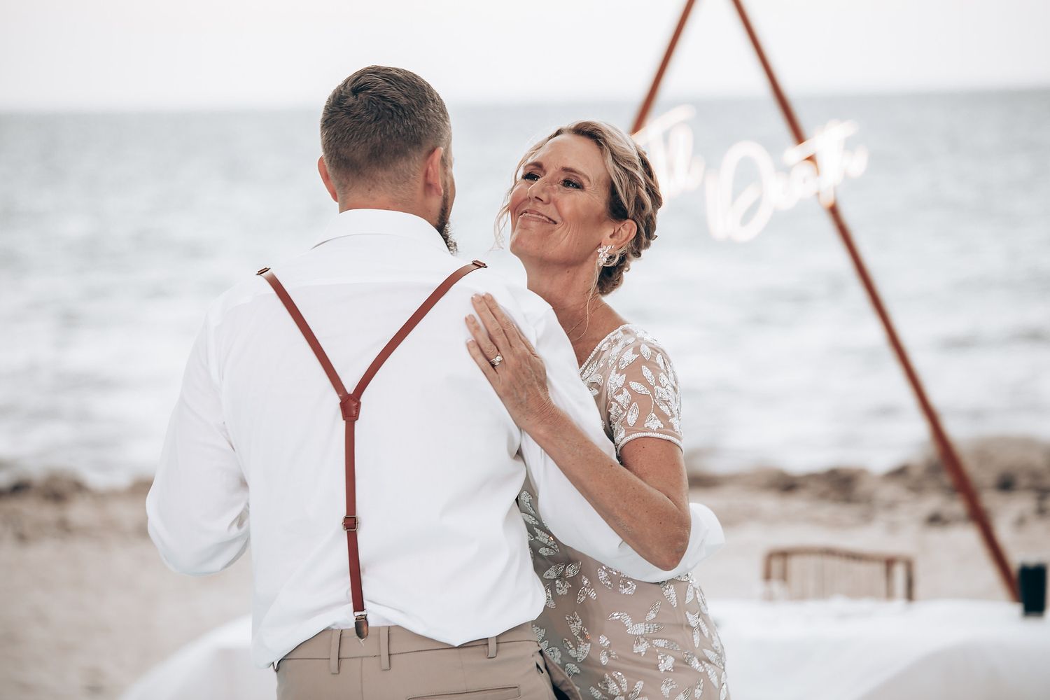 Couple shares romantic moments near wooden triangle arch on beach.