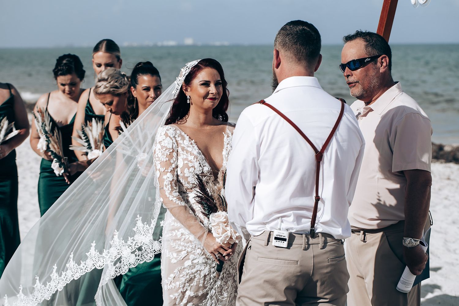 Wedding party gathered on a sunny beach with ocean waves in the background.