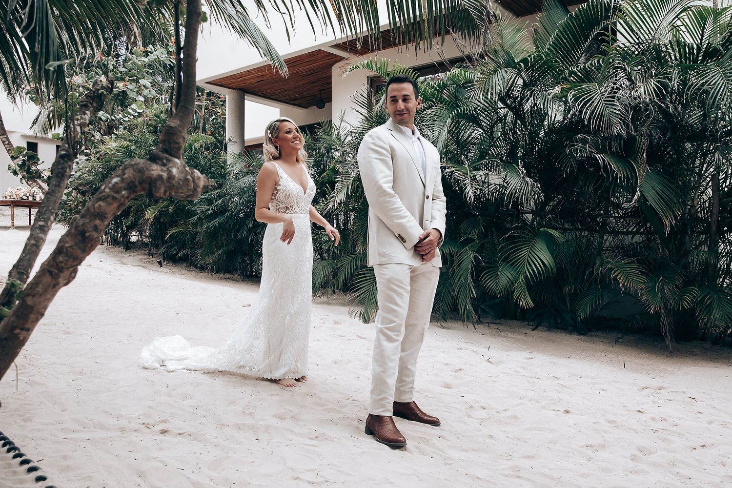 Wedding couple walking together on sandy beach path lined with palm trees.