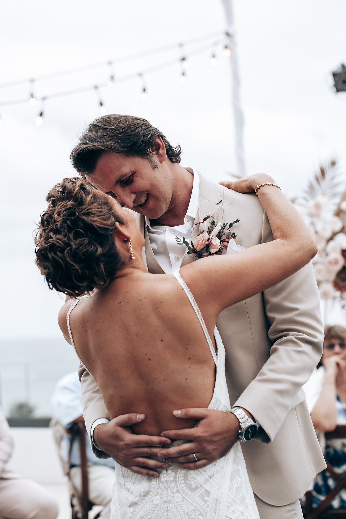A tender moment shared between a couple dancing at their wedding reception with string lights overhead.