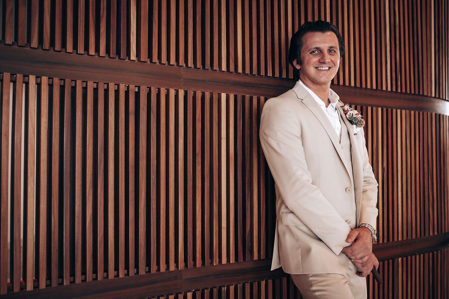 Wedding party members in white suits standing against a wooden paneled wall.