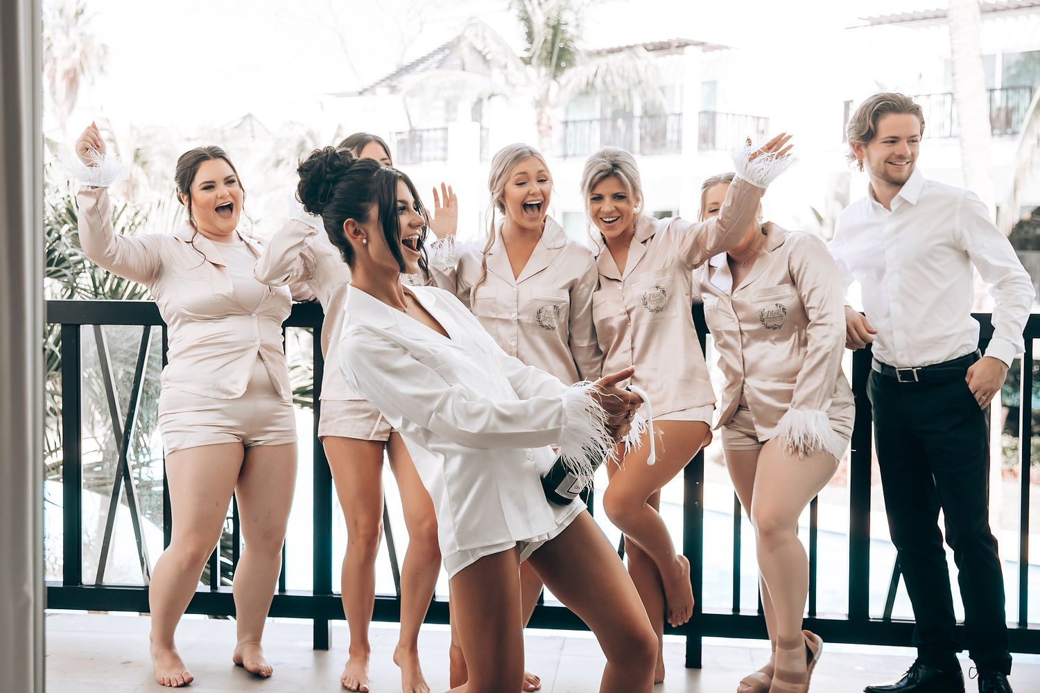 Bridesmaids in matching white robes pose playfully together in a bright room.
