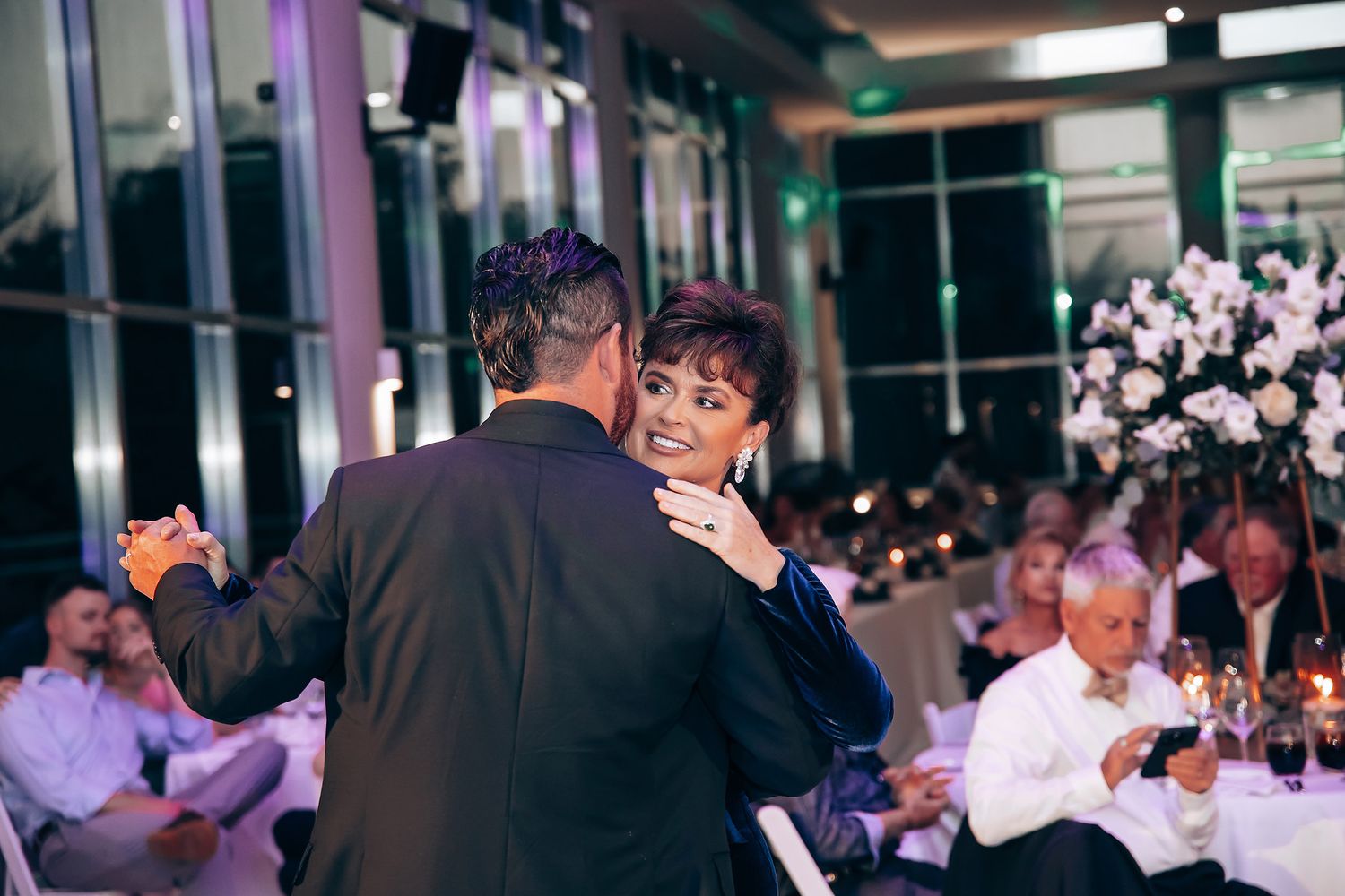 Wedding guests dancing and celebrating at an evening reception with purple mood lighting.