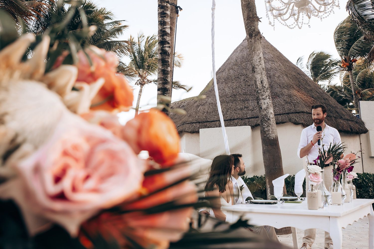 Wedding reception decor with pink roses and palm trees at a beachfront tropical venue.