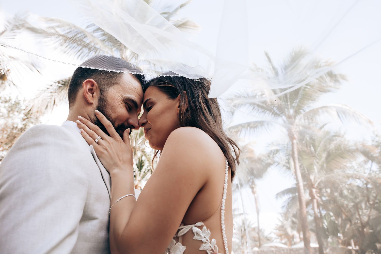 A romantic couple shares an intimate moment under swaying palm trees at a tropical beach wedding.