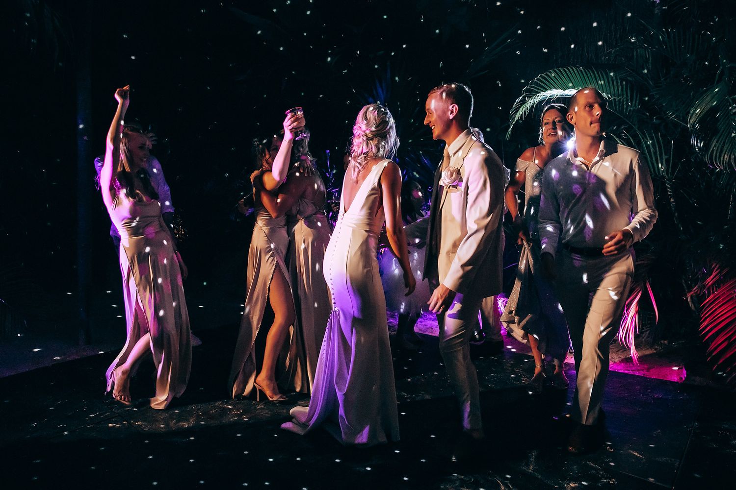 Wedding party dancing in a line during evening reception with purple lighting effects.