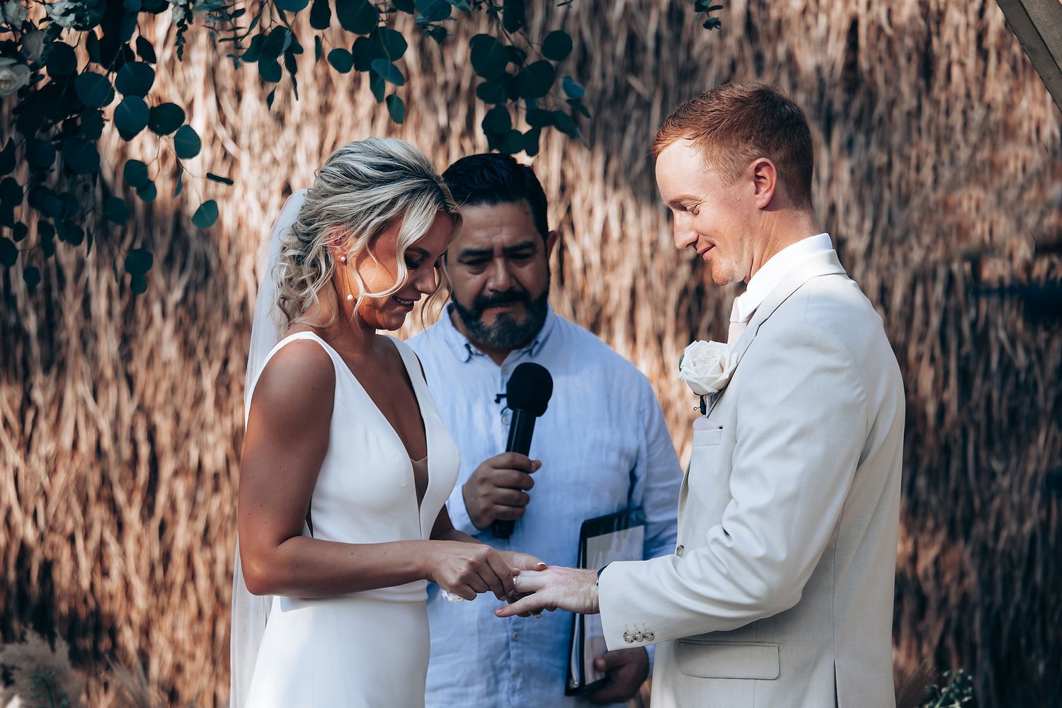 An intimate wedding ceremony moment captured under a rustic thatched canopy with natural lighting.