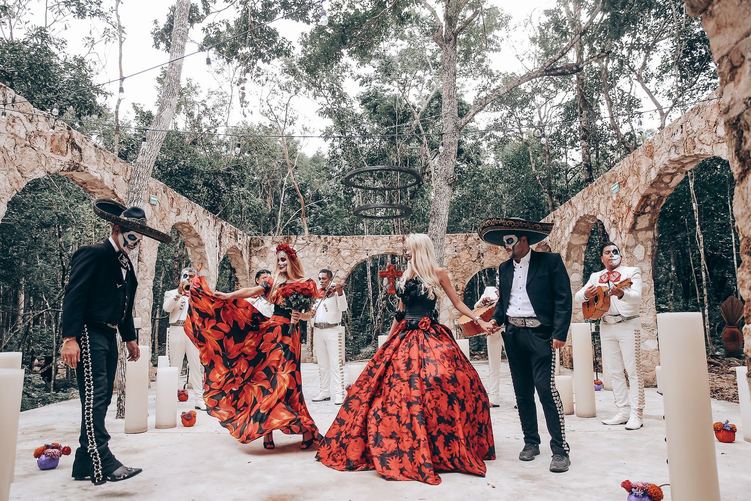 A wedding ceremony in a stone archway garden with flowing red floral dresses and mariachi musicians.