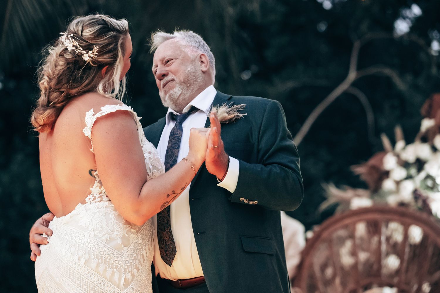 Bride and older man share a tender first dance at an outdoor wedding ceremony.