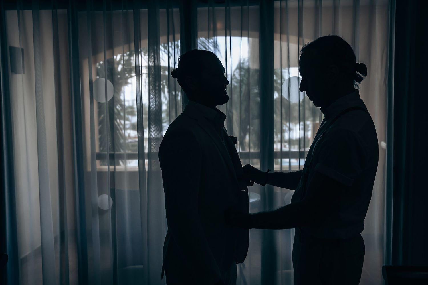 Silhouettes of people standing in a row against a window with sheer curtains creating a dramatic backlit effect.