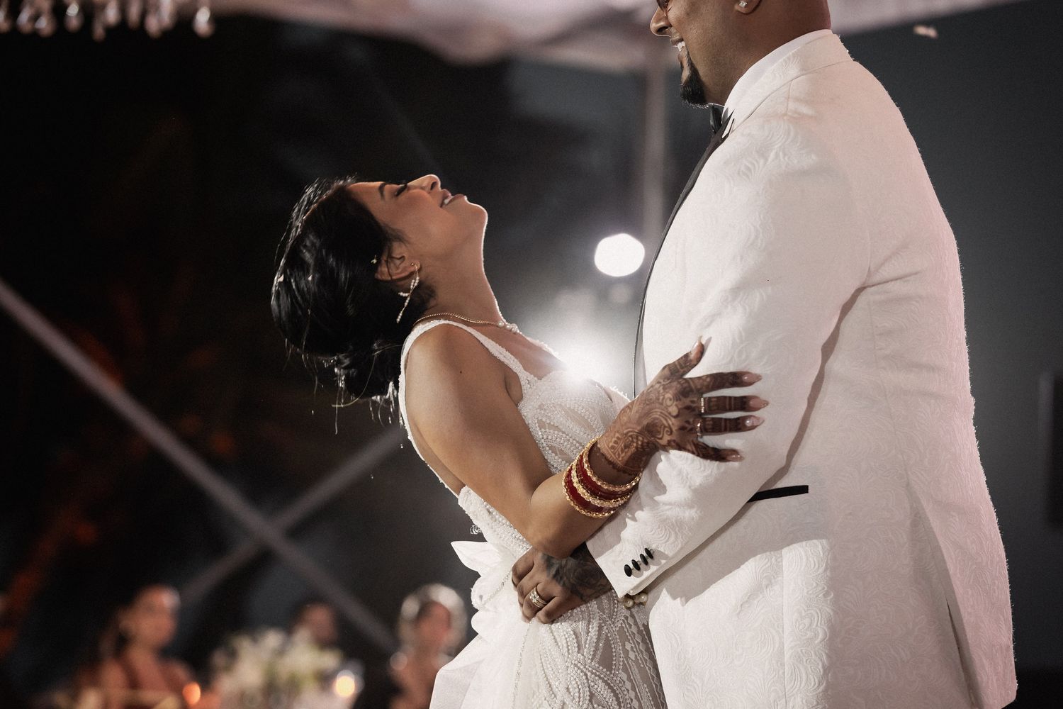 Bride in white gown with mehndi-adorned hands dances with groom at romantic wedding reception.