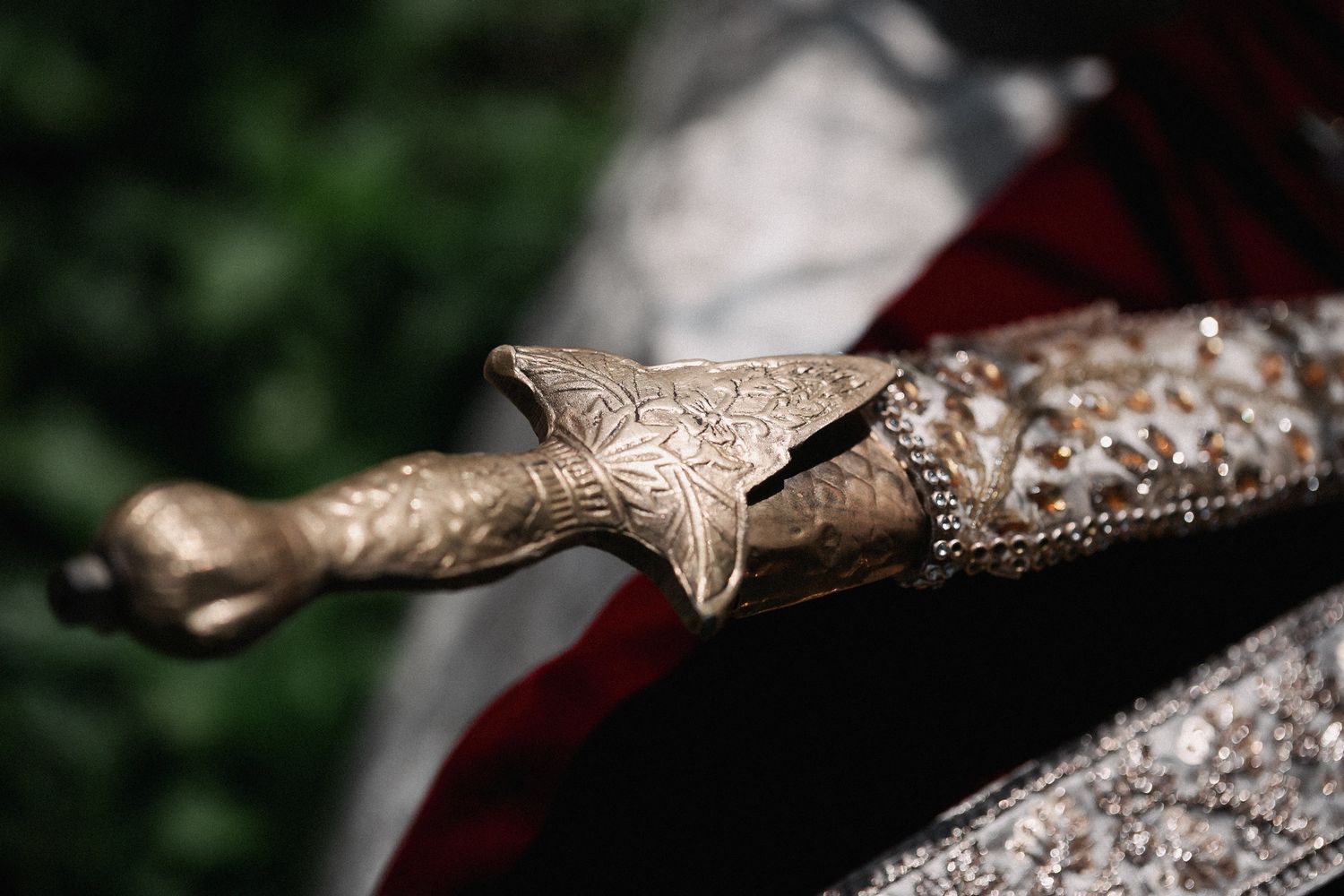 Ornate antique dagger with intricate gold engravings resting on a decorative silver surface with red fabric background.