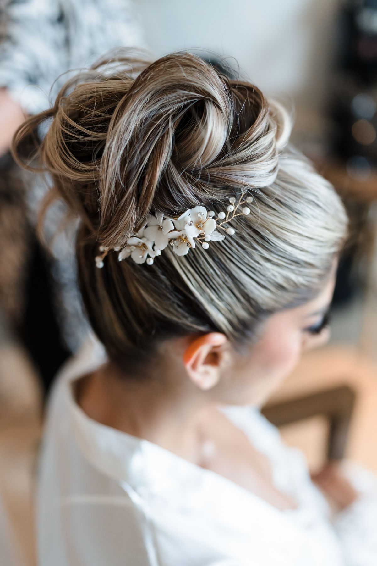 Elegant bridal updo with white floral hair comb accessory, showcasing a twisted high bun hairstyle.