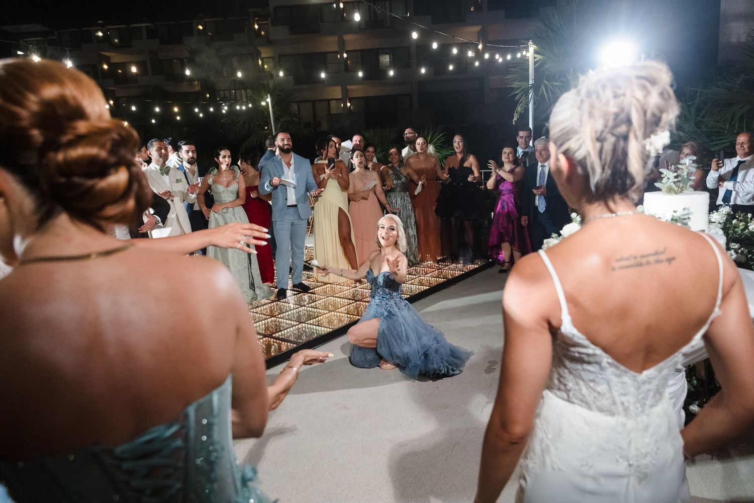 Wedding guests celebrate on dance floor as bride in blue gown dances at elegant outdoor evening reception.