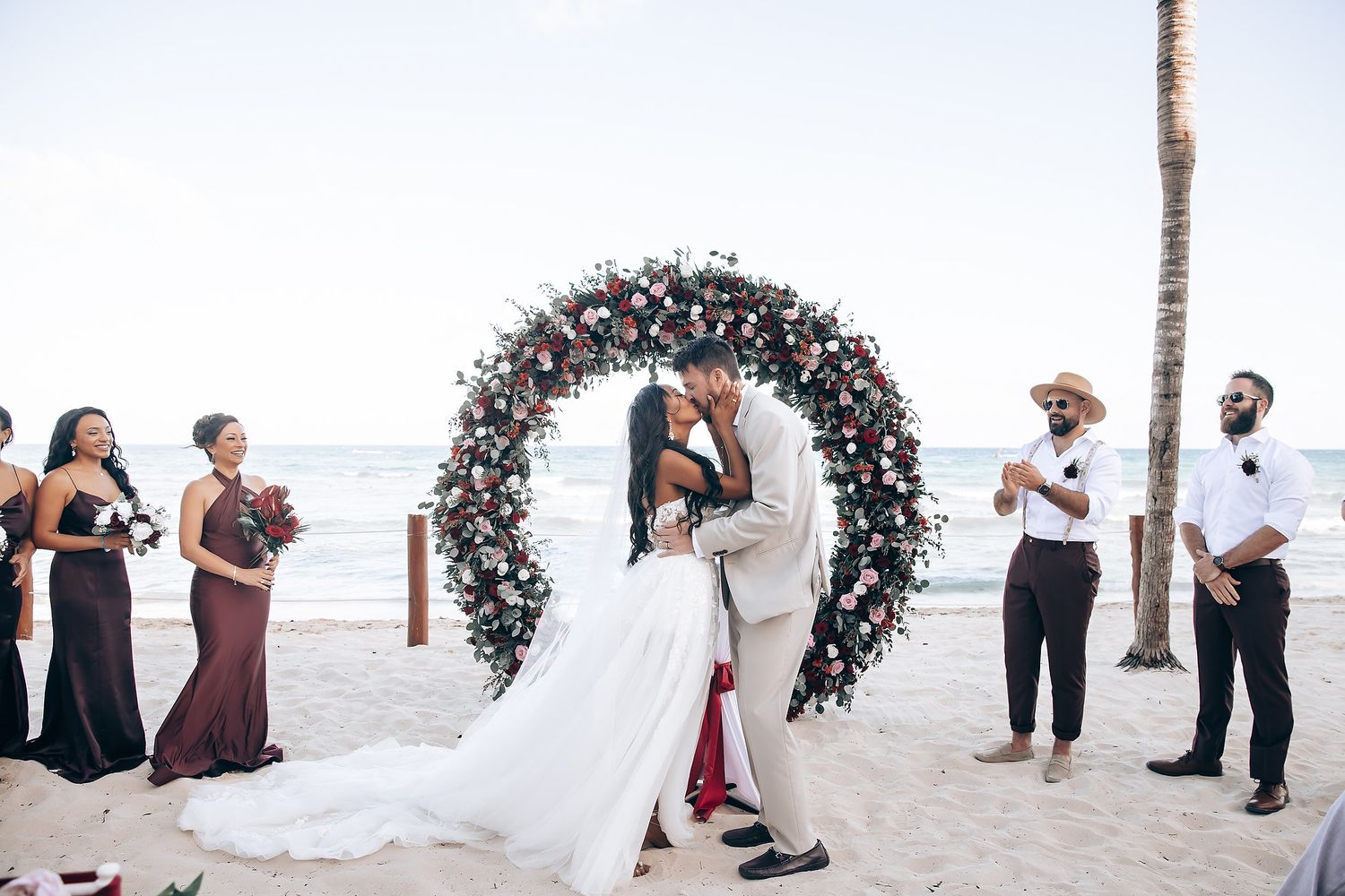 Wedding ceremony setup on white sand beach with floral arch and palm trees.