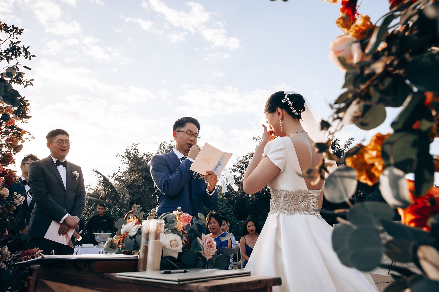 Outdoor wedding ceremony with orange floral decorations and guests taking photos.