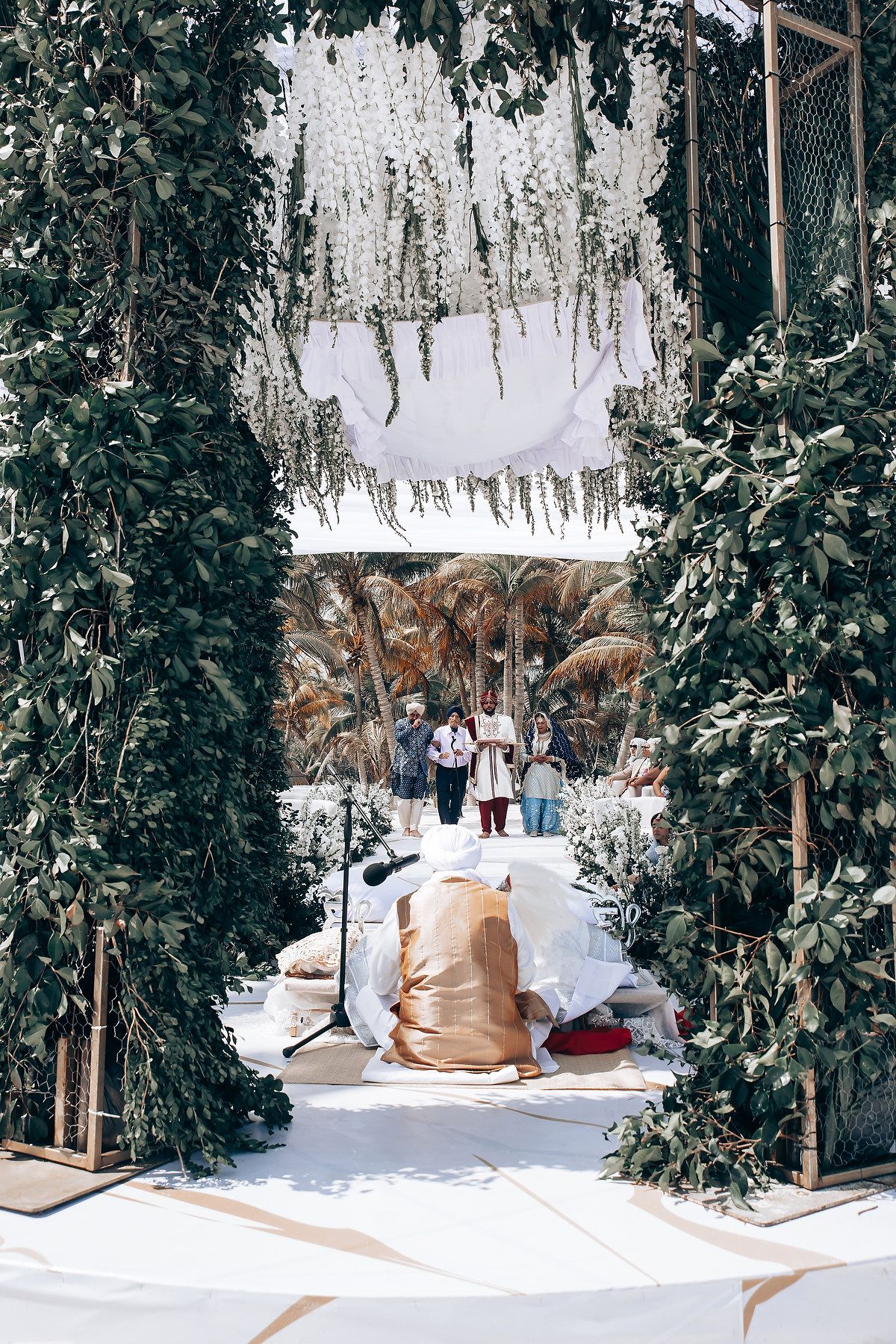 Elegant outdoor wedding venue decorated with white drapes and tropical greenery.