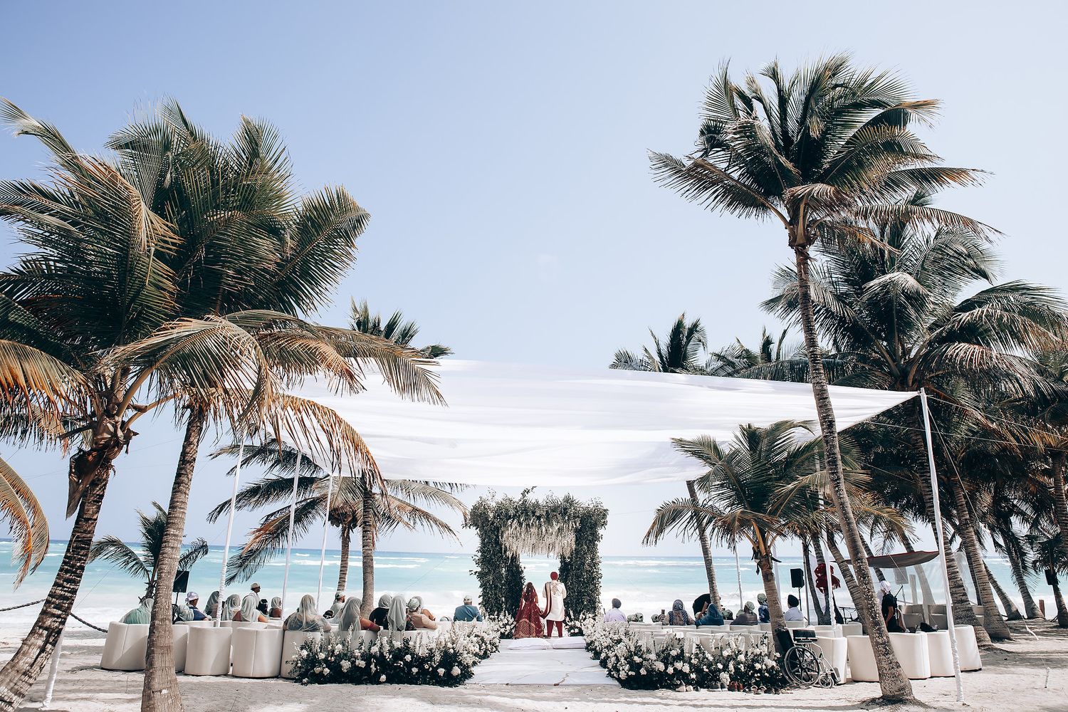Tropical beach wedding venue with palm trees lining the sandy shore against blue sky.