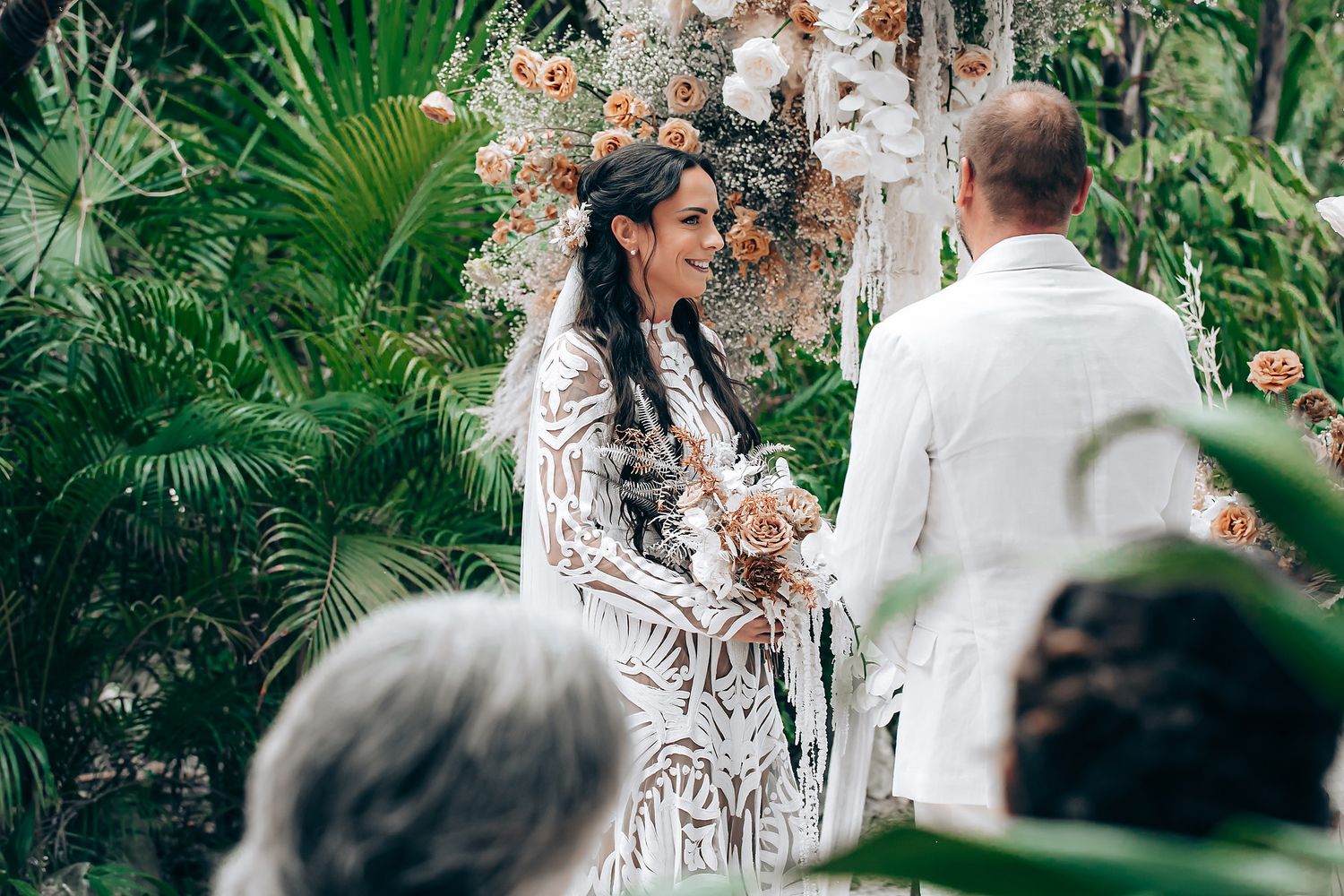 An intimate outdoor wedding ceremony surrounded by lush tropical greenery and floral arrangements.
