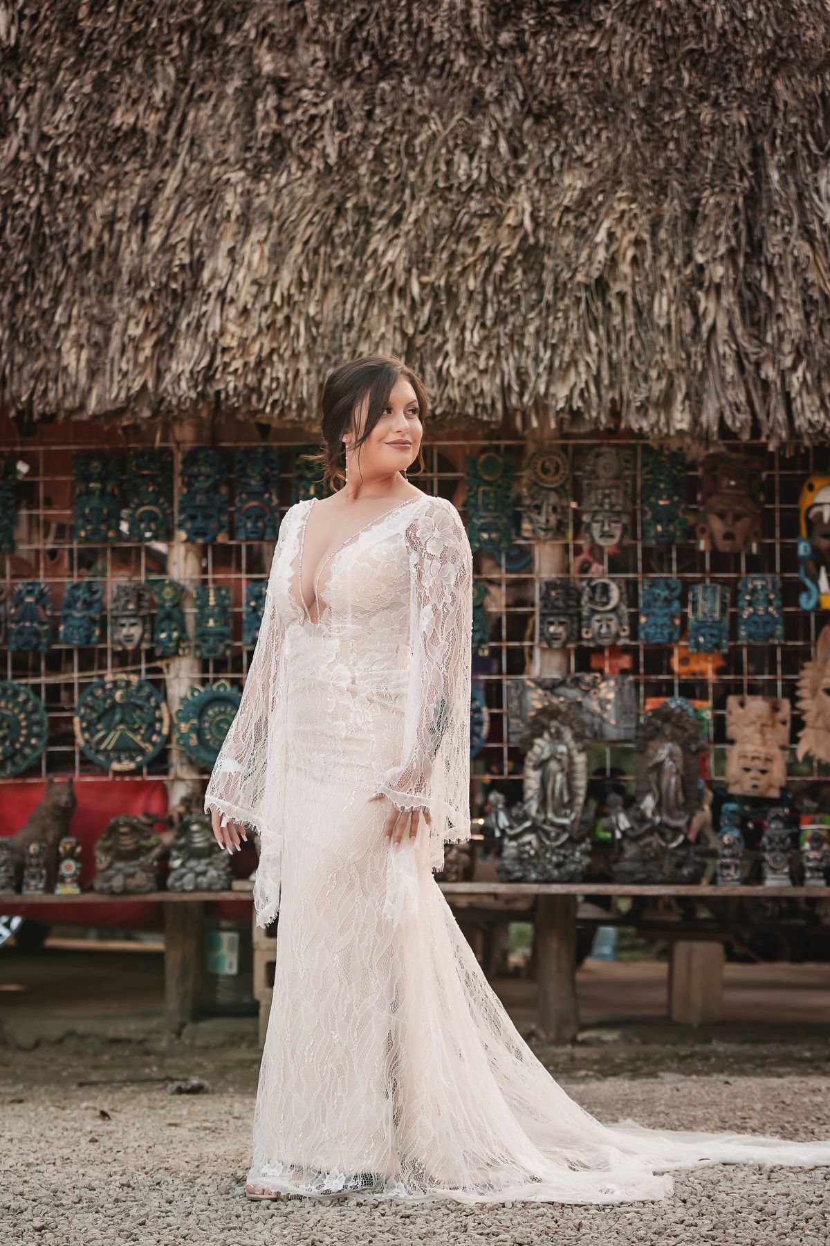 An elegant wedding dress with long lace sleeves and a flowing train captured against a rustic backdrop.