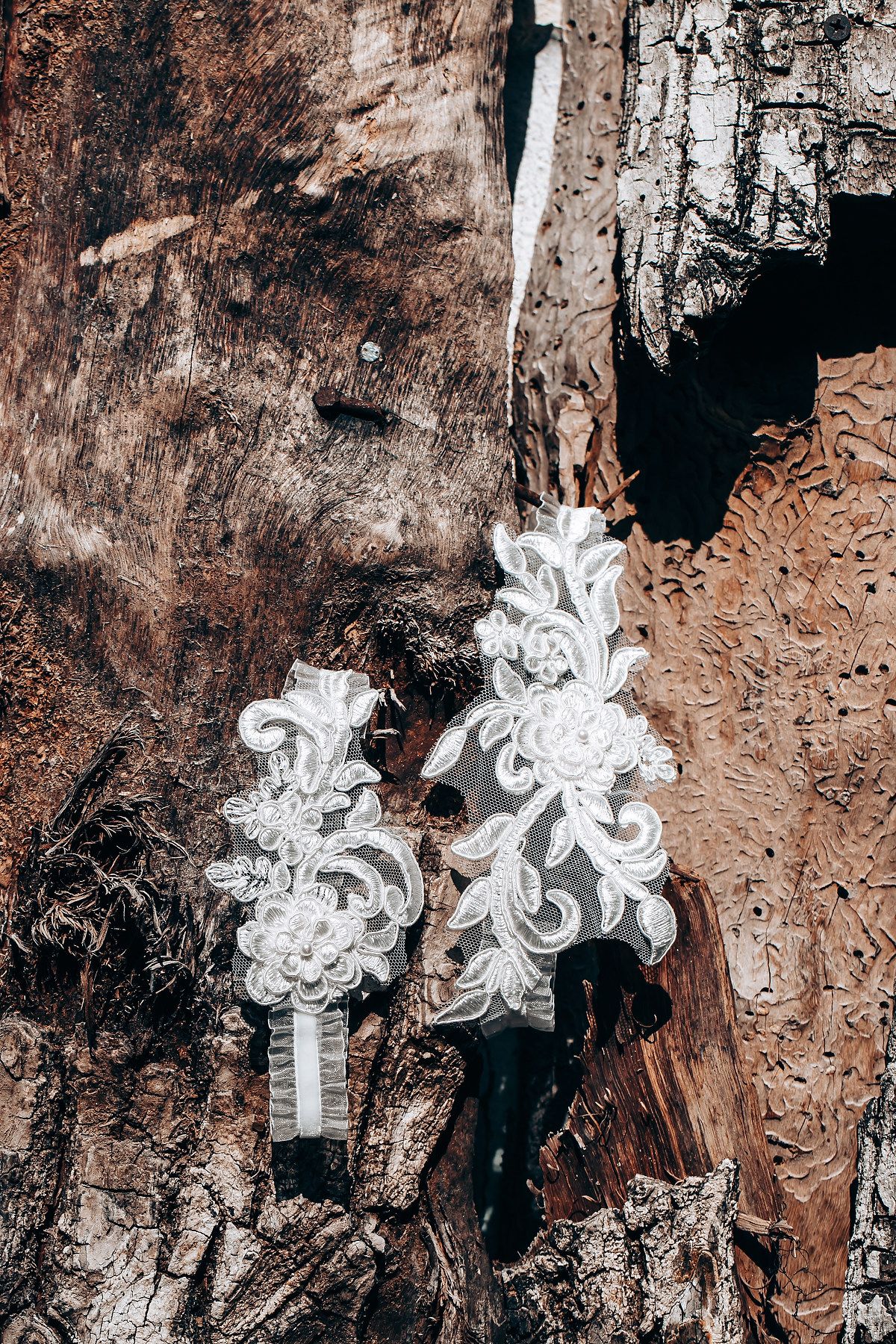 Two ornate white lace garters with floral designs hanging against a rustic wooden background.