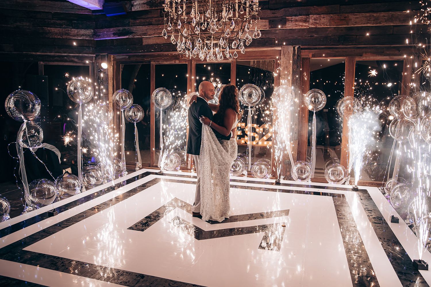 Crystal chandeliers sparkle above an elegant wedding venue with a polished white dance floor and dark decor.