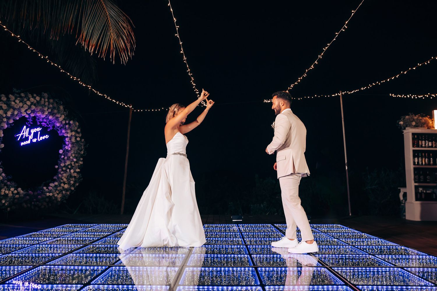 Wedding couple dances on illuminated LED dance floor under string lights at night.