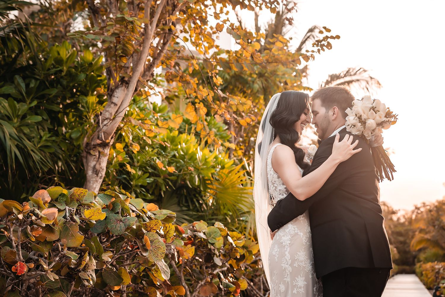 Newlyweds embrace among autumn foliage during sunset.
