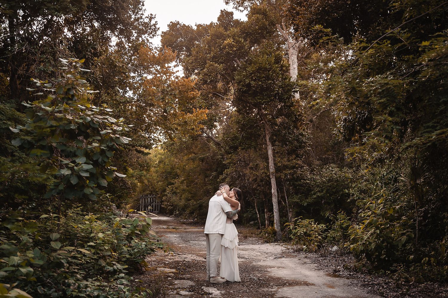 Two people stroll down a winding dirt path through a lush wooded area.