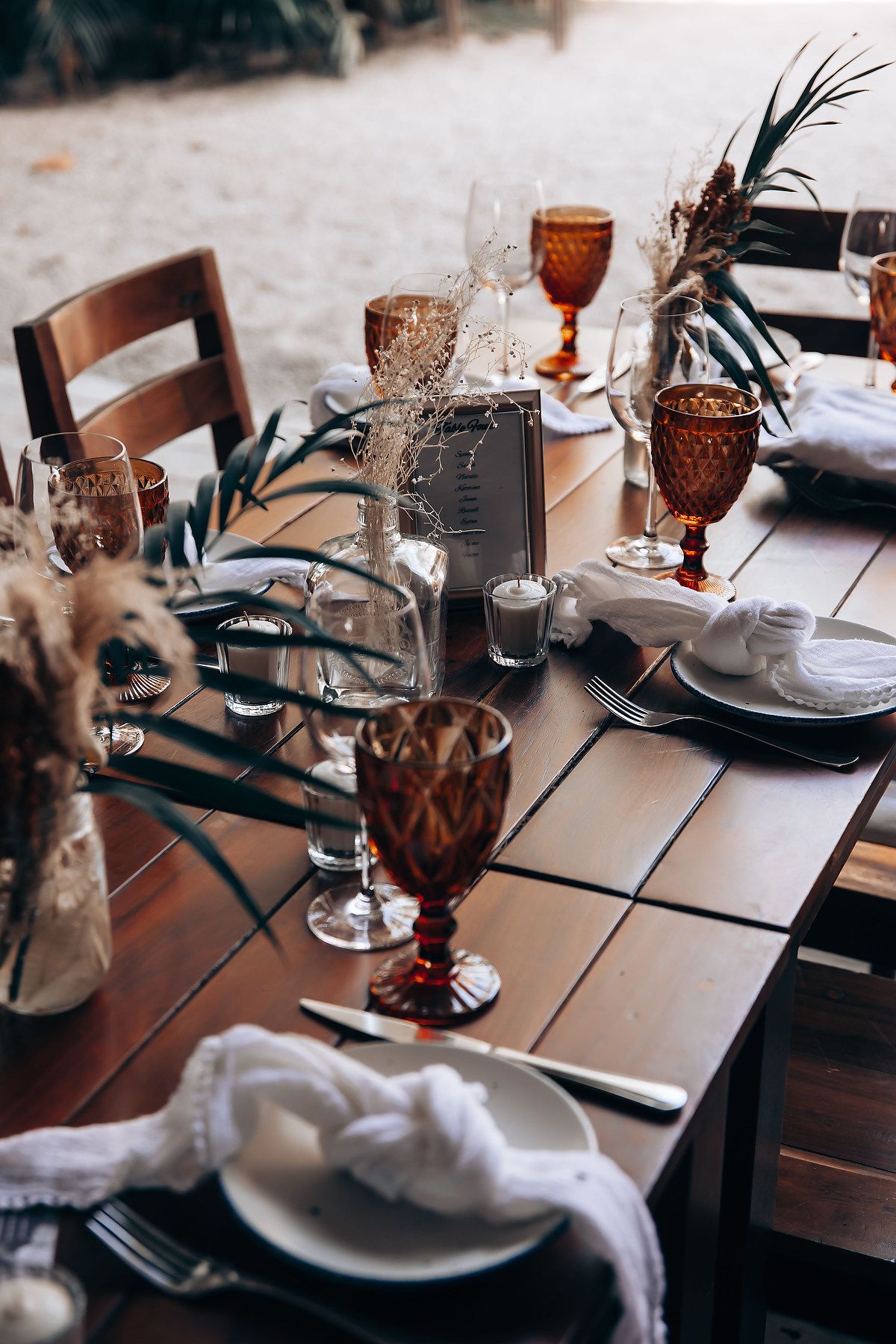 Elegant table settings with amber-colored glasses and white napkins arranged on a dark wooden dining table.