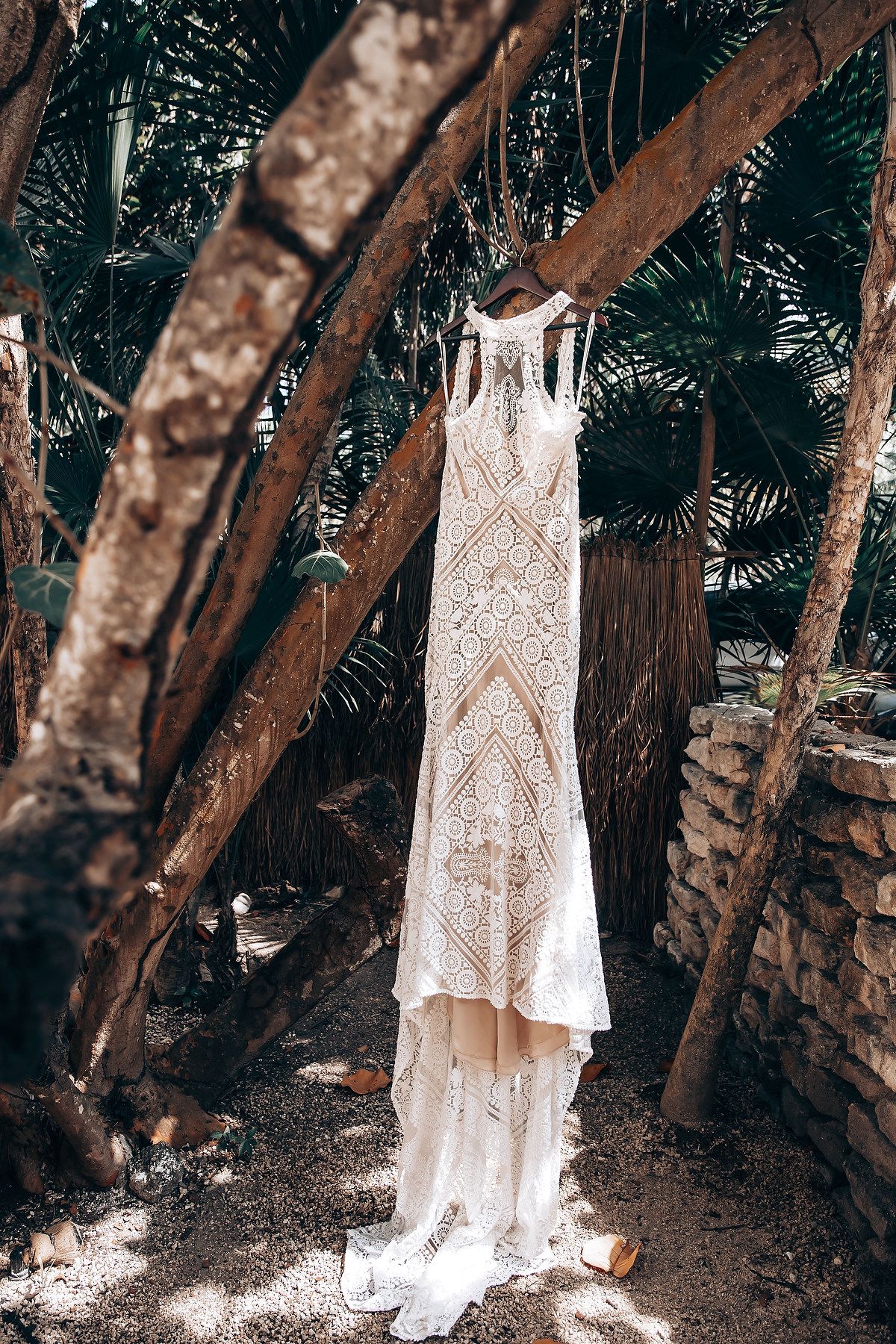 A white lace dress hangs elegantly from tree branches in a forest setting, creating a dreamy woodland atmosphere.