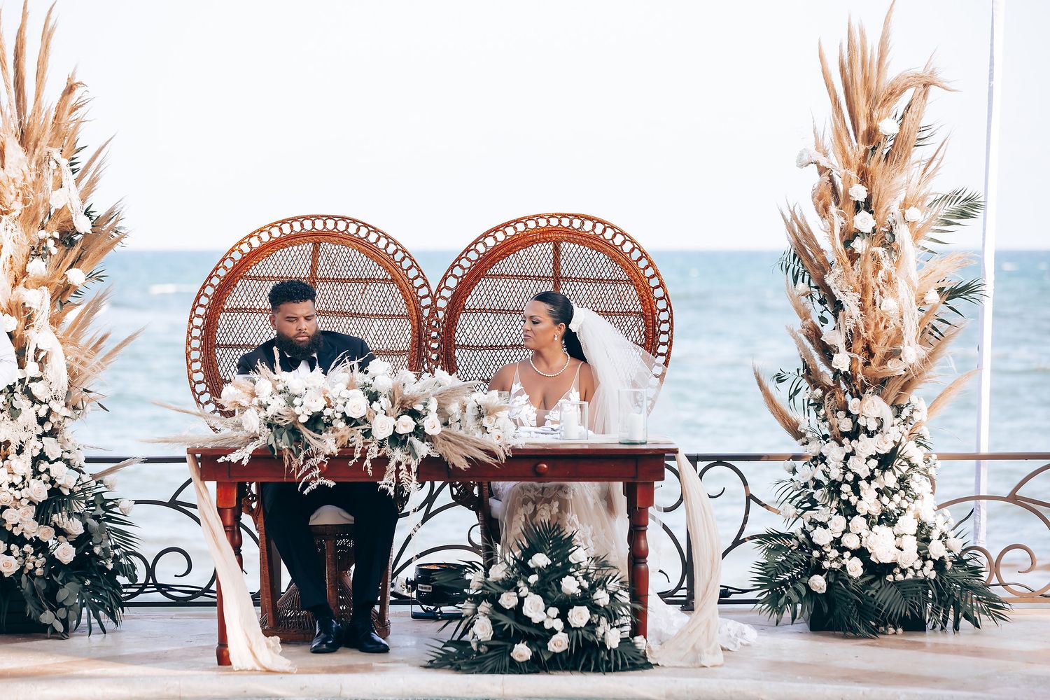 Wedding arch decorated with dried pampas grass and white flowers against an oceanfront backdrop.