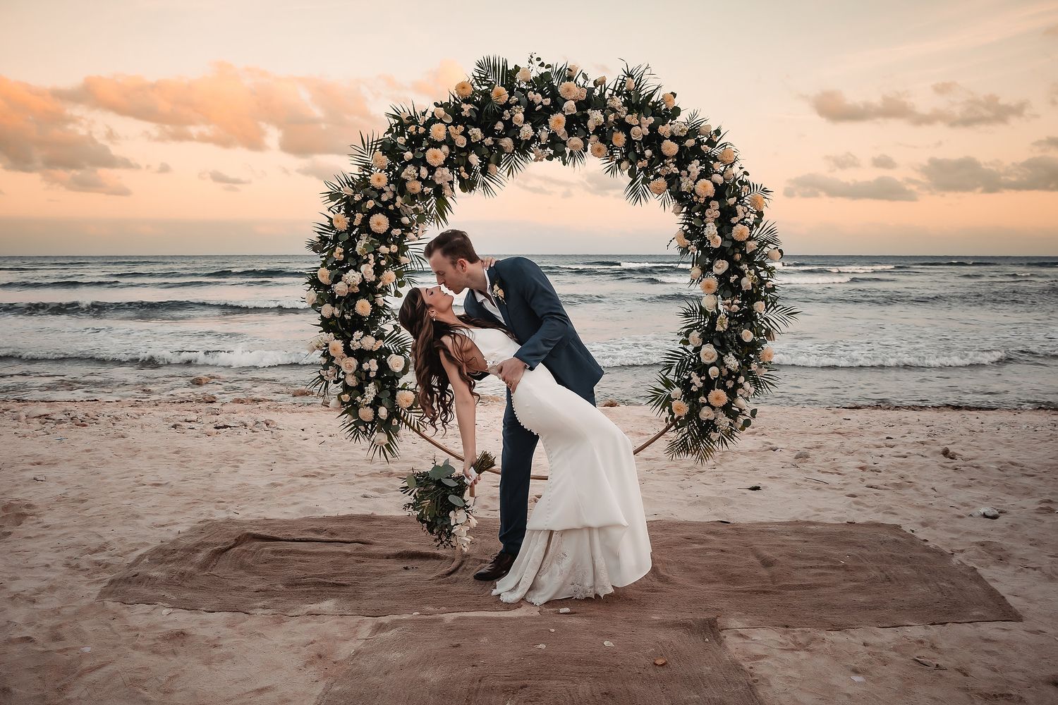Romantic sunset beach wedding ceremony with floral arch overlooking the ocean.