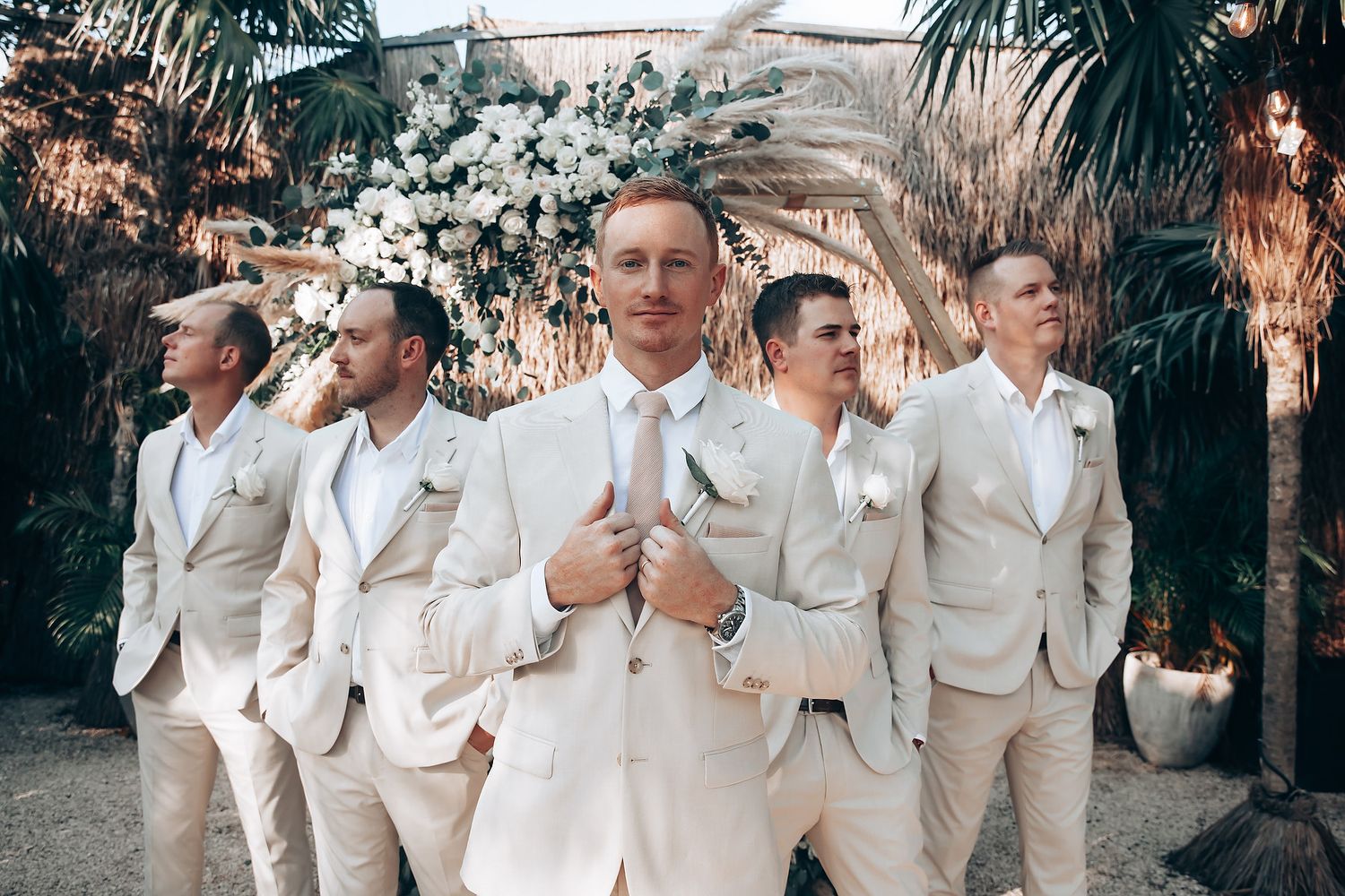 Wedding party members in cream-colored suits celebrating outdoors.