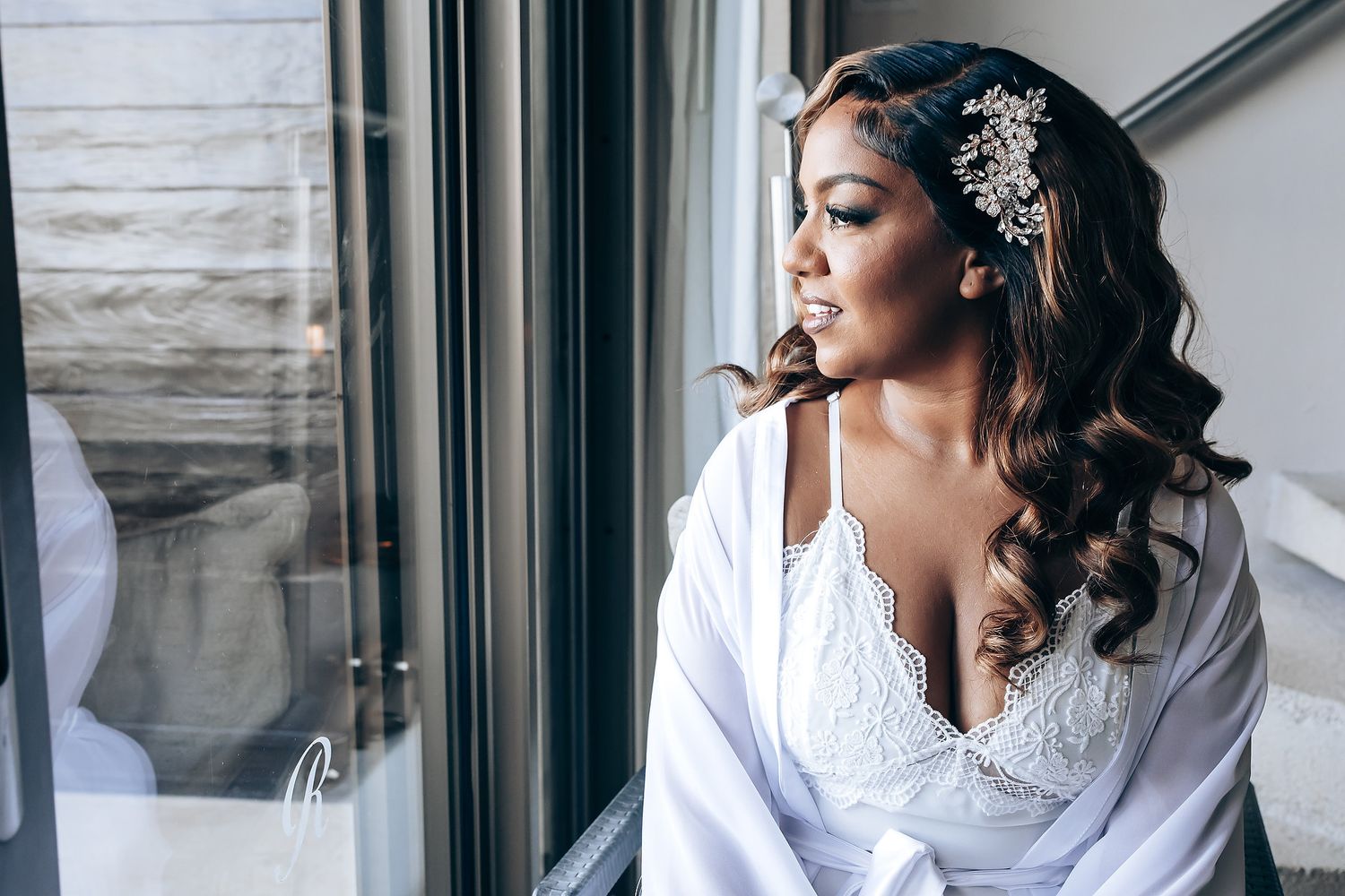 A bride getting ready on her wedding day wearing an ornate crystal headpiece and white dress.