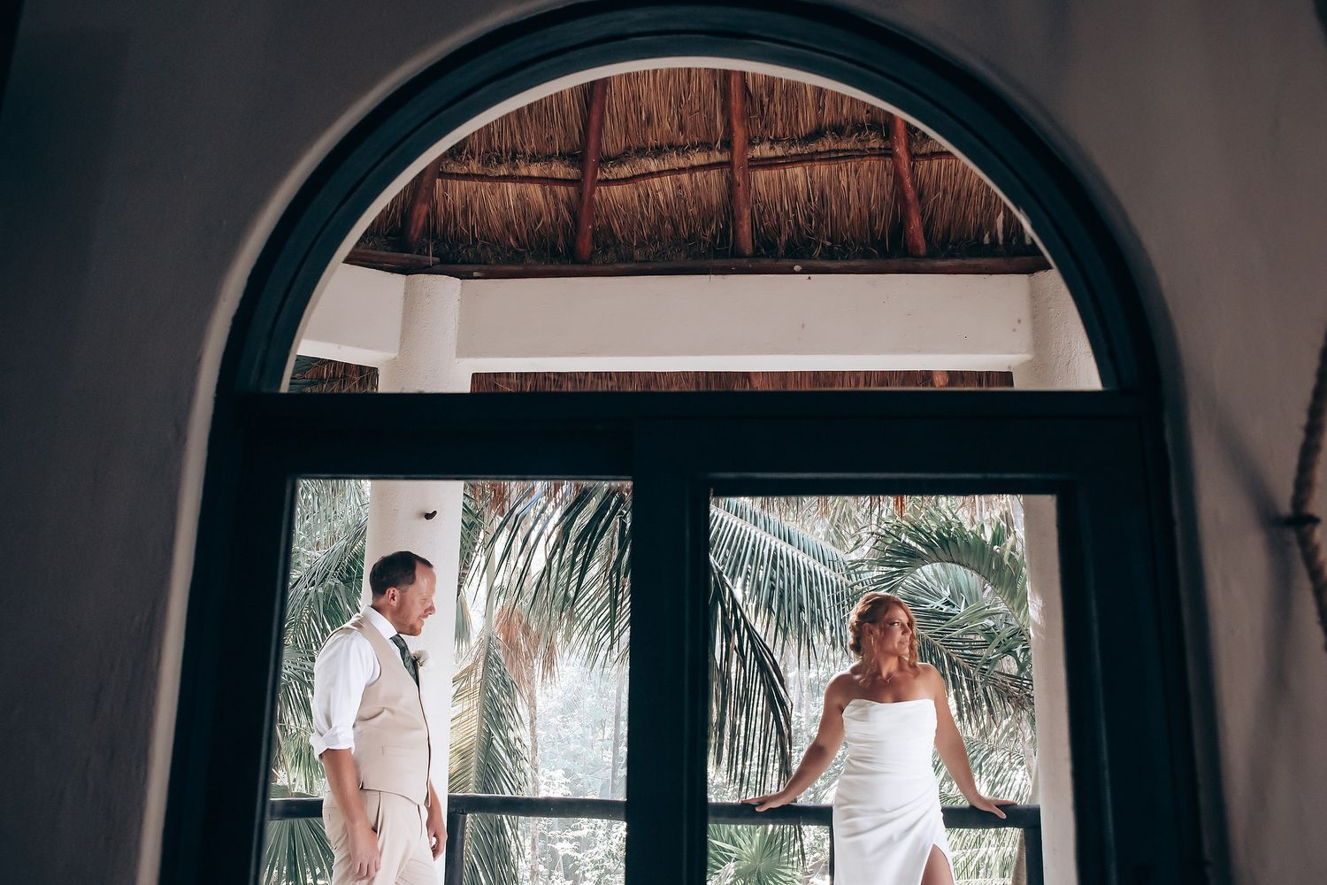 Arched doorways and windows in tropical resort setting with palm frond roof.