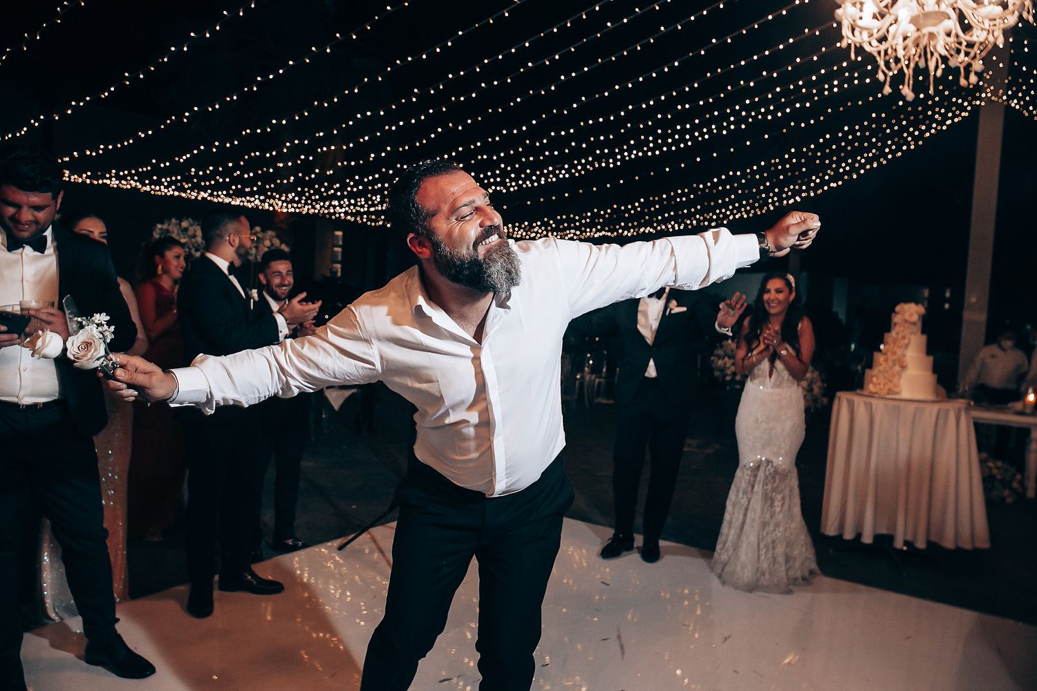 Wedding celebration with confetti falling under twinkling string lights and elegant chandeliers at an evening reception.