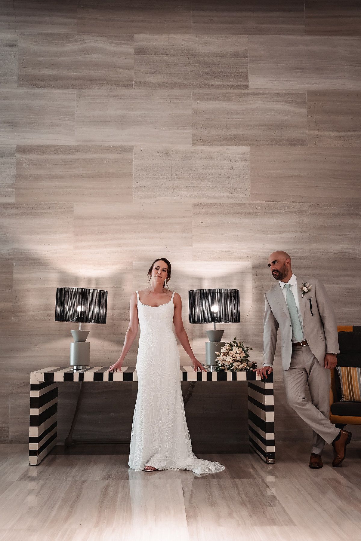 Elegant wedding portrait with a couple standing by black and white striped console tables and modern lamps.