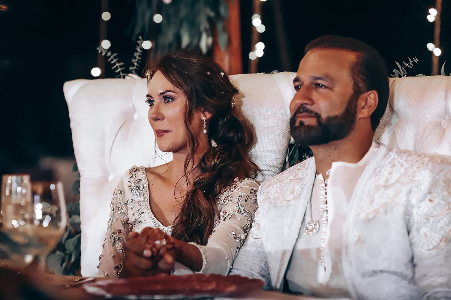 A couple in traditional Indian wedding attire share intimate moments during their reception celebration.