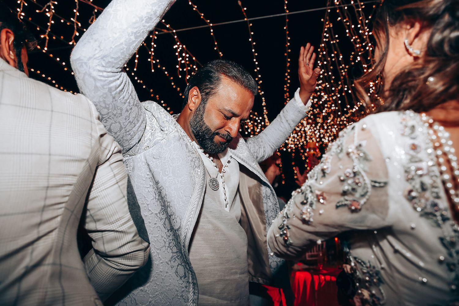 Wedding guests dance and celebrate on a dance floor with red lighting and falling confetti in the background.