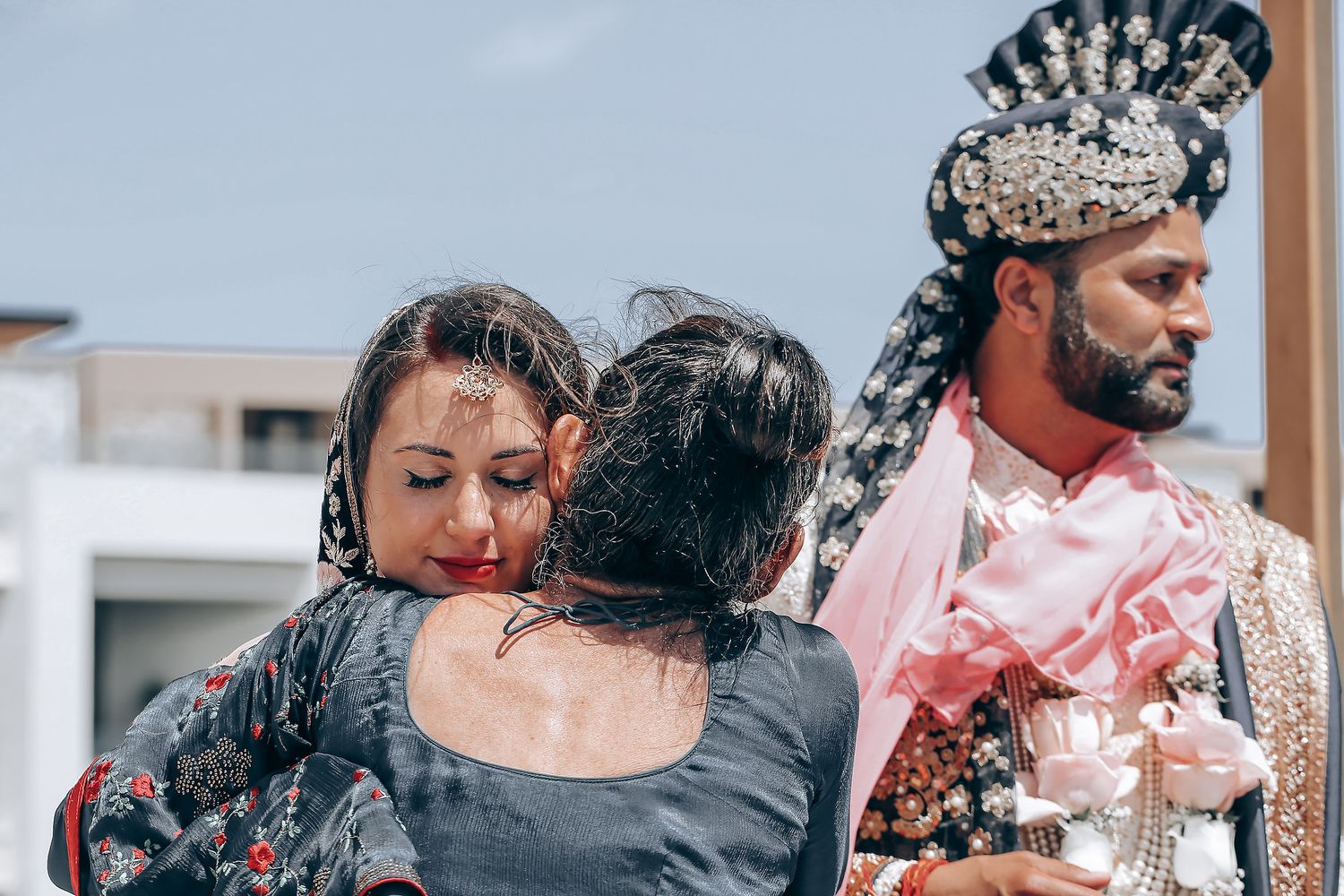 Emotional moment at a traditional Indian wedding ceremony with people embracing while wearing formal attire.