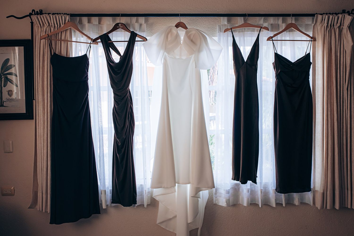 Black and white dresses hanging on a clothing rack against a white wall with sheer curtains in the background.