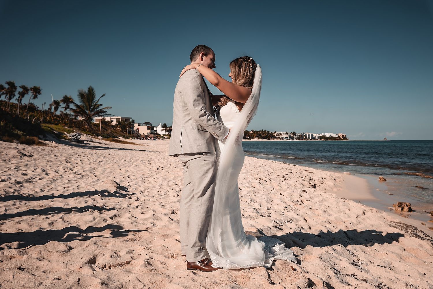 Romantic beach wedding ceremony with couple walking along the sandy shoreline at sunset.