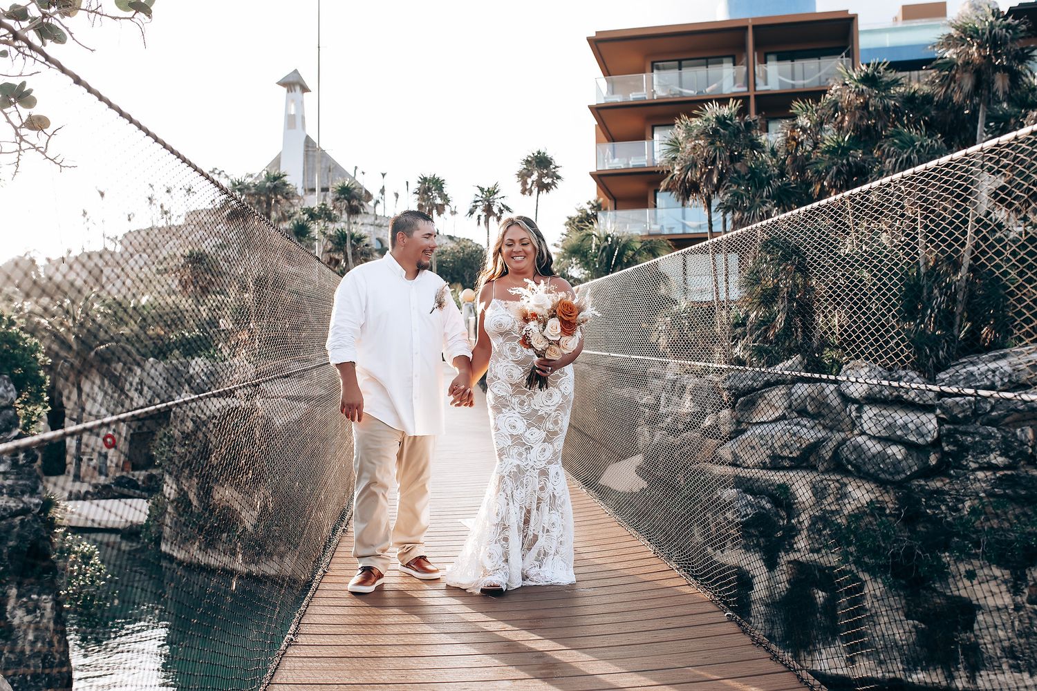 Couple walking along a wooden bridge pathway near tropical rock formations and ocean views.