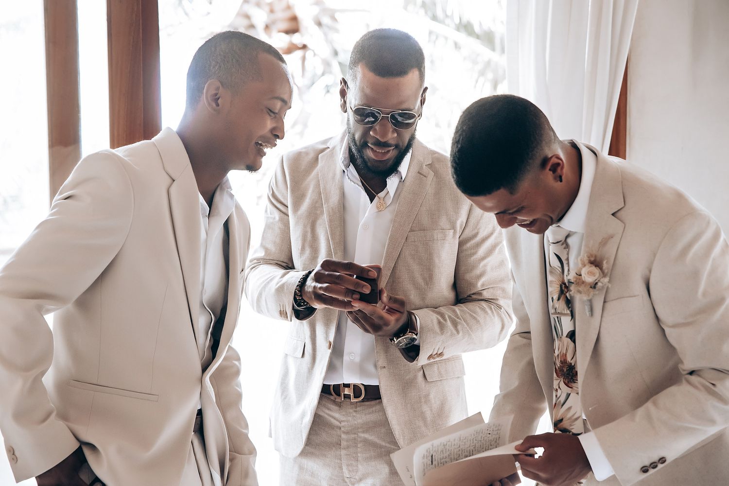 Groomsmen in white suits sharing candid moments during wedding preparations.