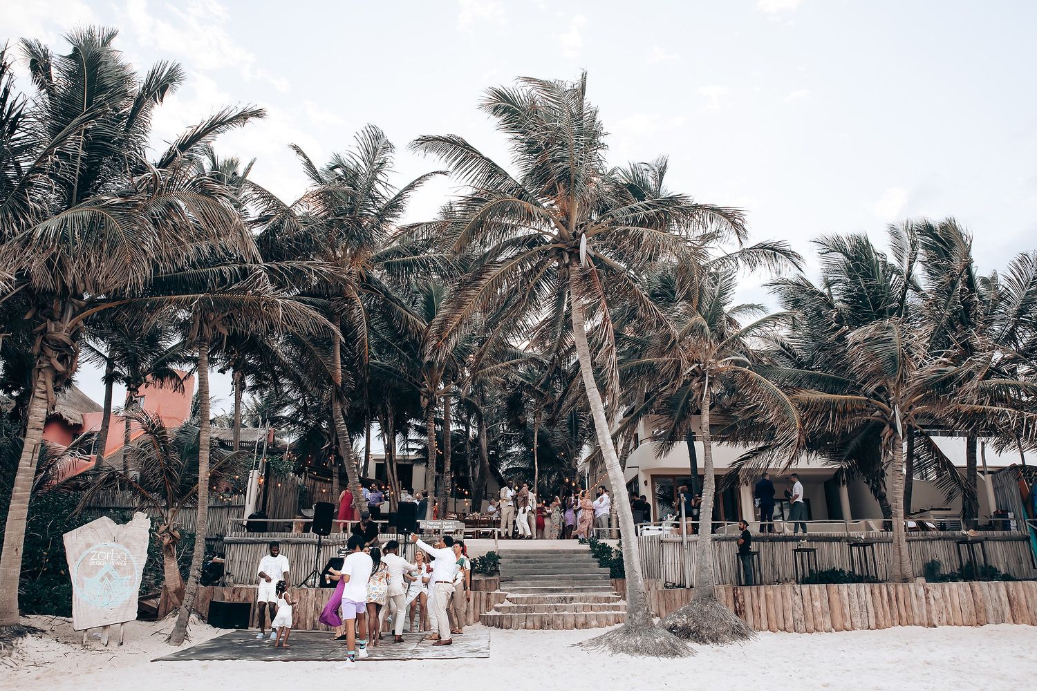Palm trees line a tropical beach setting with rustic wooden fences.