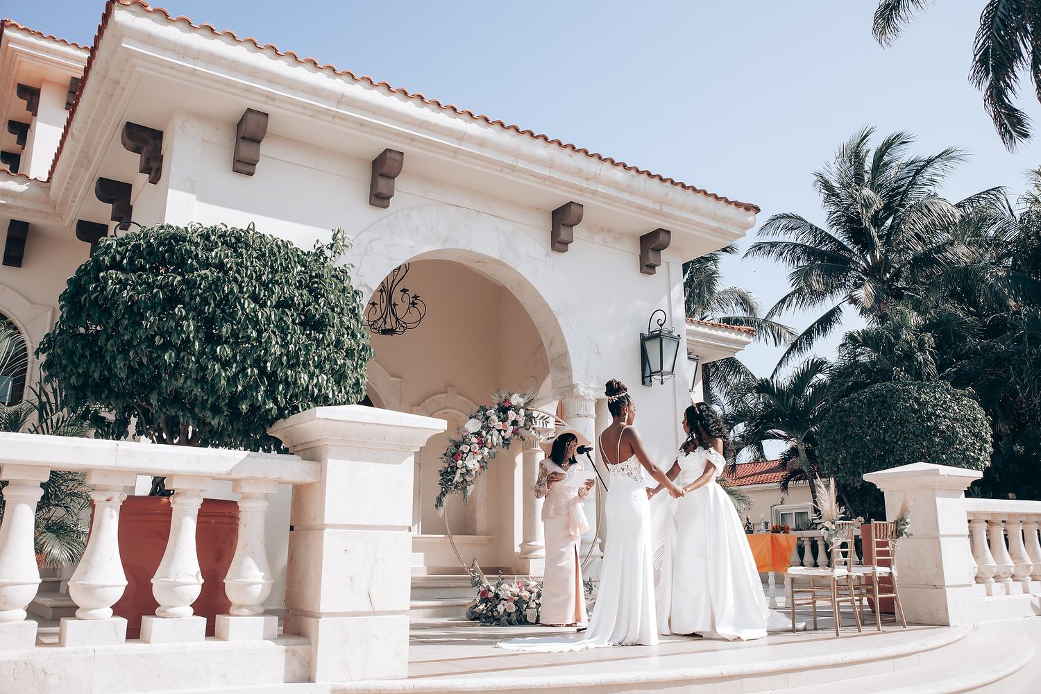 Panoramic view of a Spanish colonial style wedding venue with palm trees and white columns.