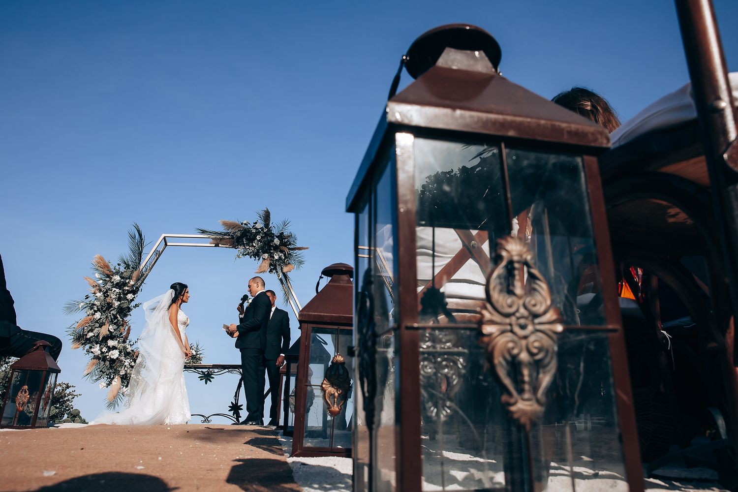 Wedding ceremony taking place outdoors with palm trees and blue sky in the background.