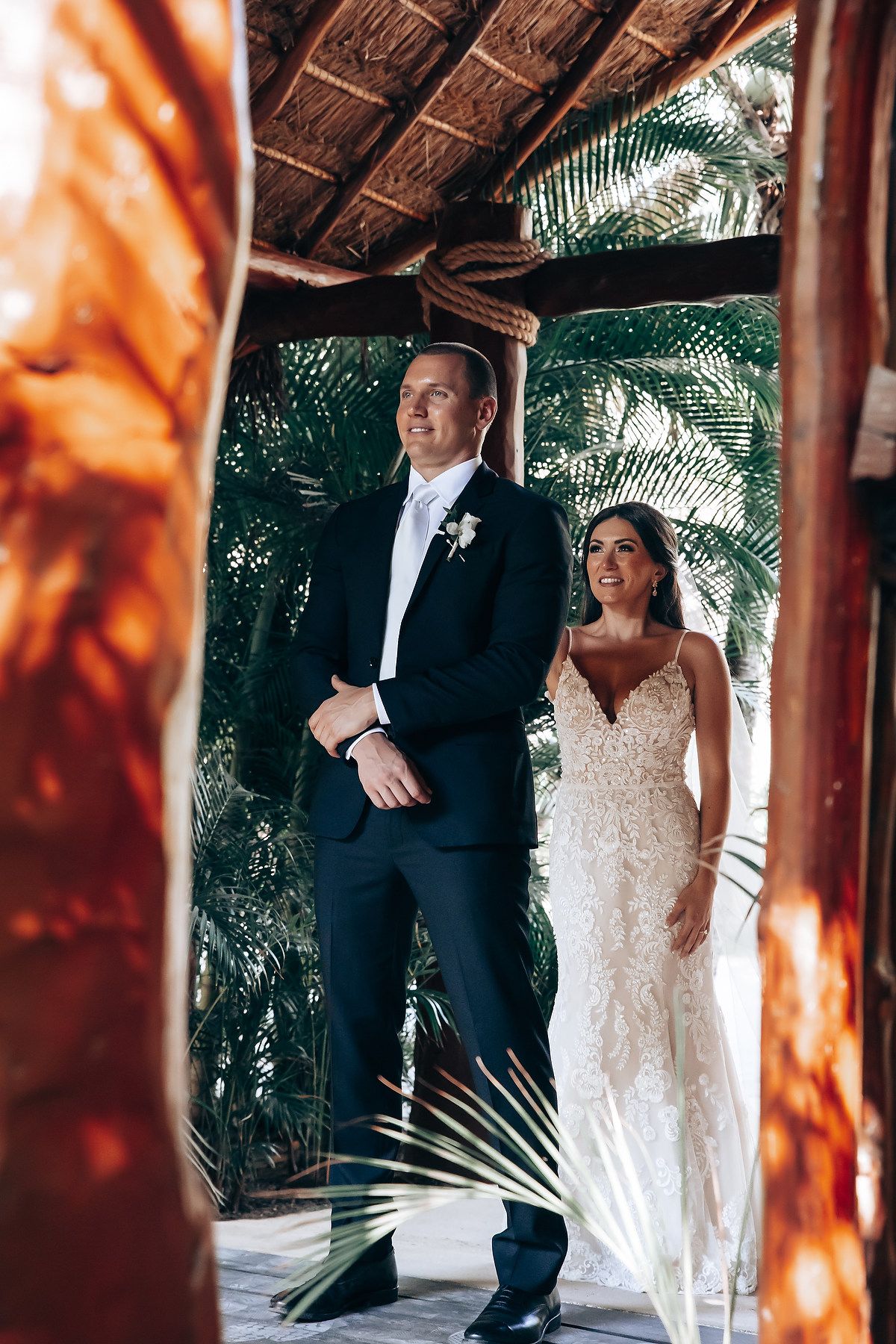 Couple sharing a romantic moment under a thatched roof palapa surrounded by tropical foliage.